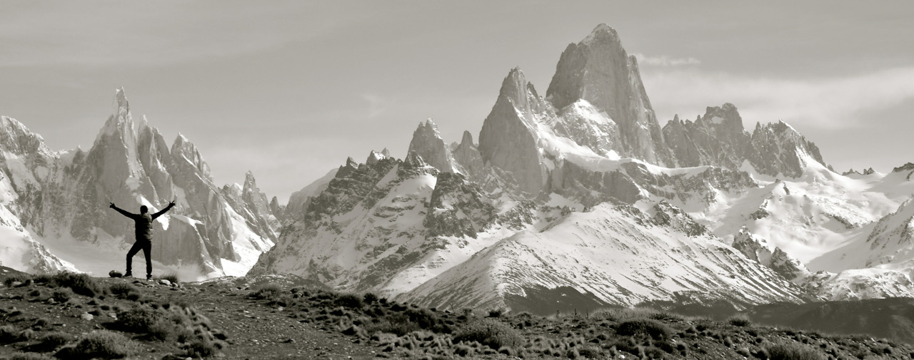 Archival black-and-white panorama of Fitz Roy, with Jeff standing small on the left, arms open beneath the mountains